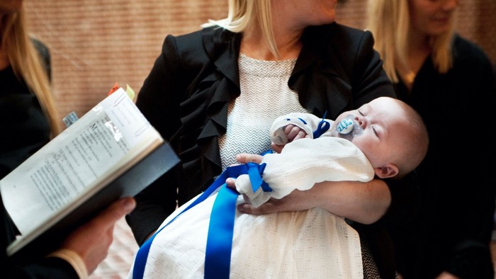En kvinde holder et barn, mens en mand læser fra en bog