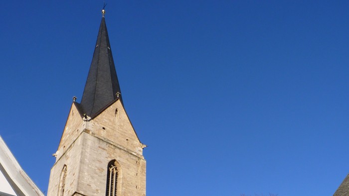 Kirche mit hohem Kirchturm und Uhr vor blauem Himmel.