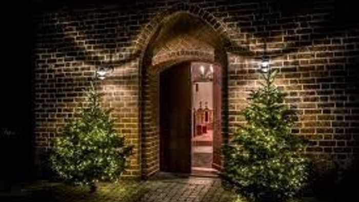 En lyset mur med en indgående dør omgivet af grønne planter.