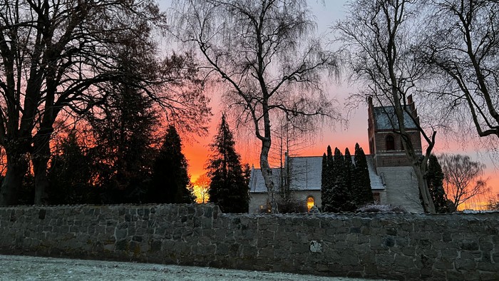 En solnedgang bag en stenmur og træer med en kirke i baggrunden