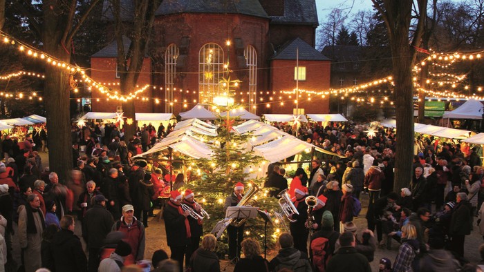 Weihnachtsmarkt vor Kirche mit vielen Menschen und Lichterketten