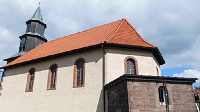 Kleine Kirche mit rotem Dach und Turm, umgeben von bewölktem Himmel