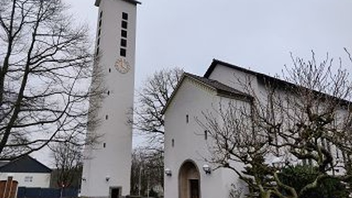 Weiße Kirche mit hohem Turm und Uhr, umgeben von kahlen Bäumen.