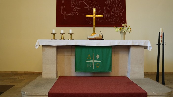 Eleganter Altar mit einem Kreuz, Kerzen, Blumenschmuck und einem grünen Tuch mit religiösen Symbolen.
