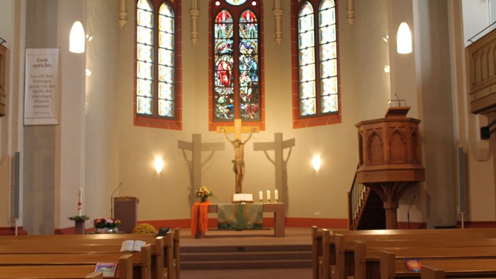 Innenraum einer Kirche mit Altarraum und Buntglasfenster