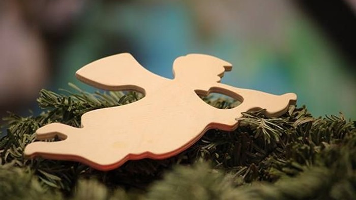 Ein hölzernes Engel-Dekoration liegt auf einem grünen Tannenbaumzweig.