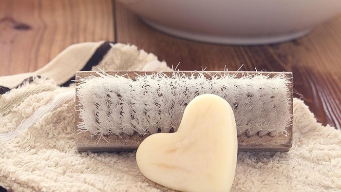 Ein herzförmiges Stück Seife liegt auf einem Handtuch neben einer Bürste und einer Schale auf einer Holzfläche.
