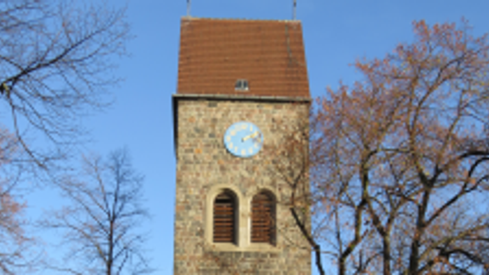 Alter Kirchturm mit Uhr und buntem Glasfenster, umgeben von Bäumen