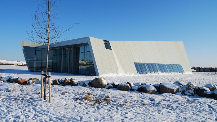 Et moderne, hvide bygning i sneklædt landskab med en træ og sten.