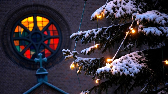 En juletree med lys og sne foran et vinduesglas med farverne orange, gul og rød