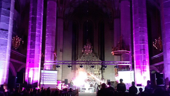 Große Kirche mit lila Beleuchtung und Menschen in den Bänken