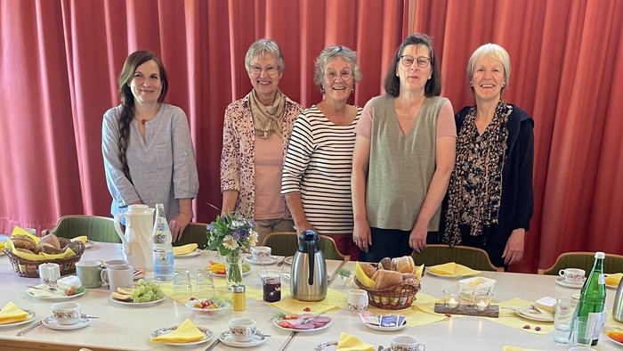 Das Team des Frauenfrühstücks steht fröhlich vor dem eingedeckten Frühstückstisch.