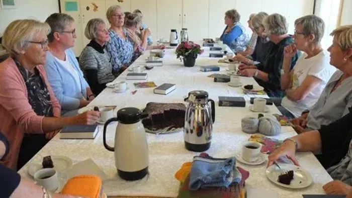 En gruppe kvinder sidder ved et bord med kaffe og kage.
