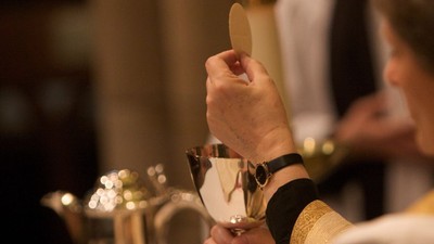 A person holding a small circular object near a teapot.