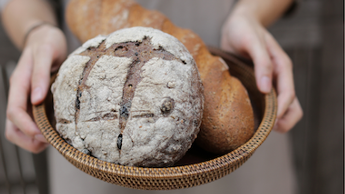 Eine Person hält einen Korb mit verschiedenen Broten und Brötchen.