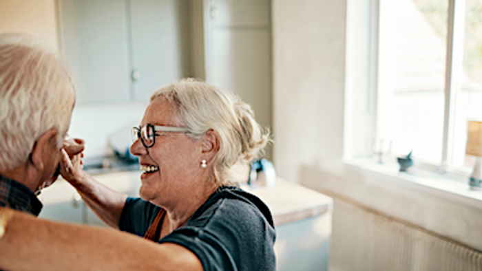 Ein älteres Paar lacht zusammen in einem hellen Badezimmer.