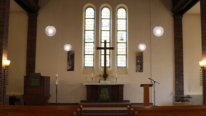 Moderne Kircheninnenraum mit einem schlichten Altar, bunten Glasfenstern und hölzernen Kirchenbänken unter sanfter Beleuchtung.