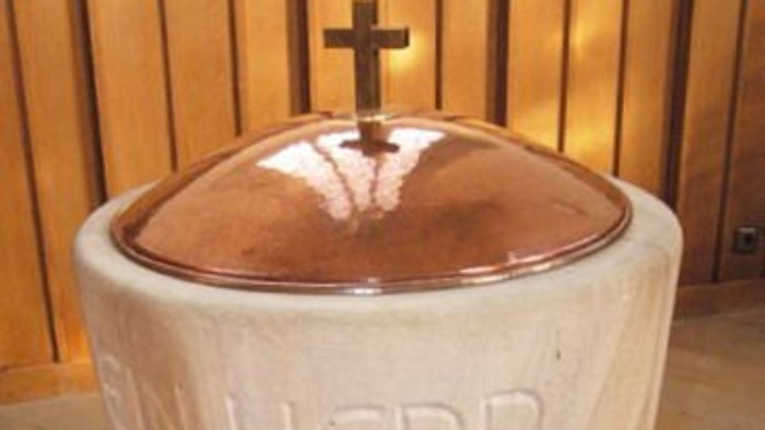 Der Taufstein mit Kreuz und lateinischer Inschrift in einer Kirche.