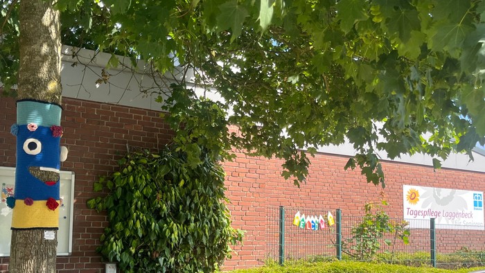 Das Foto zeigt die Tagespflege mit dem Schild und einen Baum der davor steht, der mit einem Strickmonster geschmückt ist.