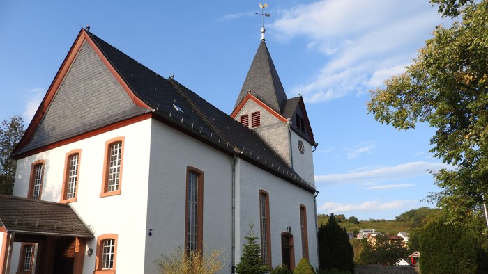 Weiße Kirche mit roter Umrandung und Kirchturm, umgeben von Grünflächen.