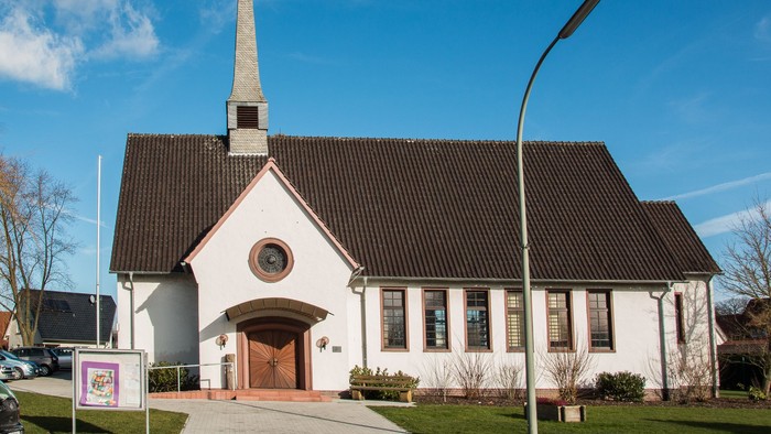 Weiße Kirche mit hohem Turm und schwarzem Dach unter blauem Himmel