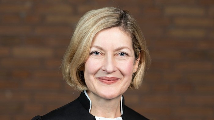 Eine Frau mit blondem Haar lächelt vor einer Ziegelwand.