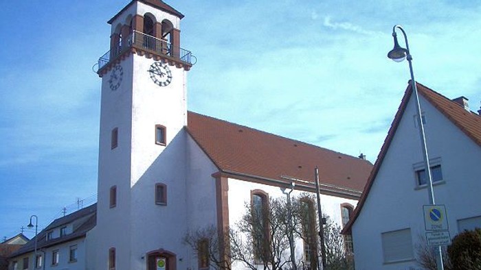 Weiße Kirche mit hohem Turm und Uhr, rote Ziegeldächer, klarer blauer Himmel