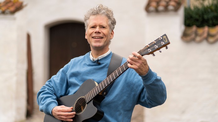 En glad mand spiller guitar på en gade.