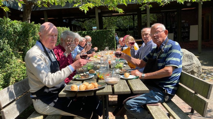 En gruppe af mennesker sidder udendørs ved en bordspise og gennytter mad og drikkevarer