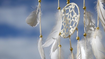Ein Traumfänger mit weißen Federn und Perlen vor blauem Himmel