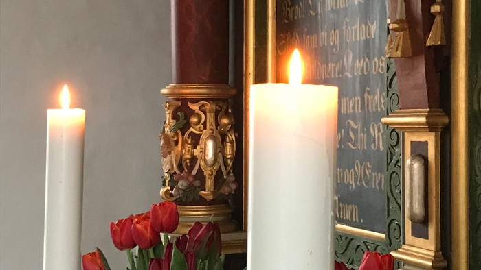 To candler, to blomsterarrangementer og en altertavle