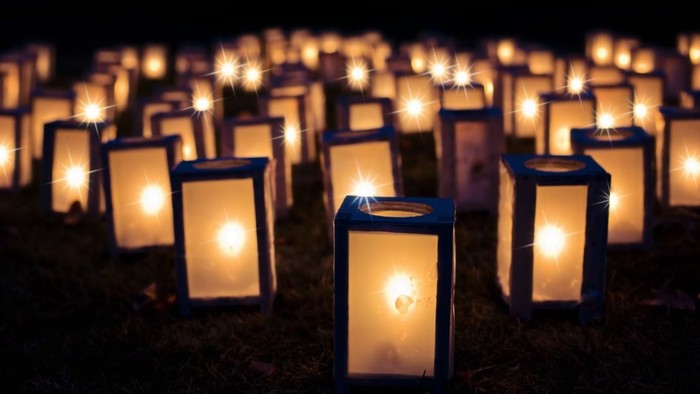 Zahlreiche angezündete Laternen, die nachts auf dem Gras platziert sind.