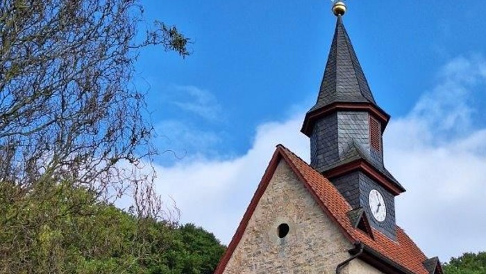 Kirche mit Uhrturm und rotem Dach, umgeben von Bäumen und einem weißen Lattenzaun.