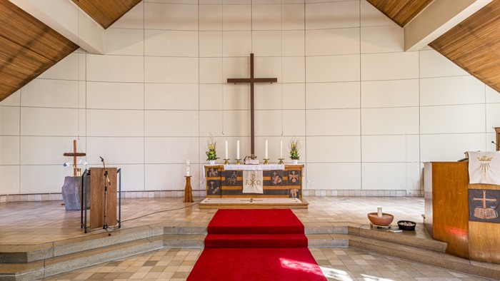 Die Kirche mit hohem Kreuz und Altar, rote Teppichrolle im Vordergrund