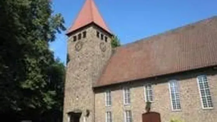Altes Steinhaus mit hohem Turm und roter Spitze, umgeben von Bäumen