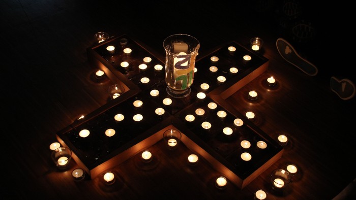 Überkreuz angeordnete Kerzenleuchter mit brennenden Kerzen und einer Glasvase in der Mitte