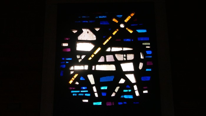 Buntglasfenster mit geometrischen Mustern und einer Taube.