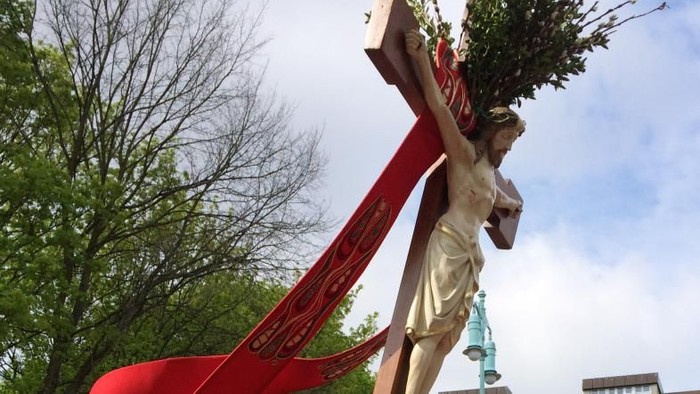 Mann in rotem Gewand, der ein Kreuz mit einer Jesusstatue trägt.