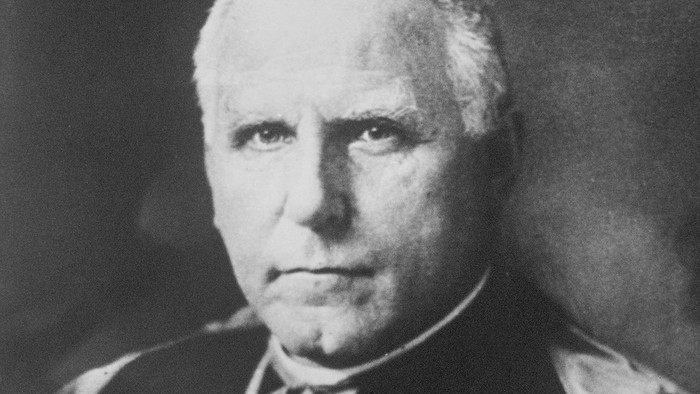 Ein älterer Mann mit weißen Haaren, der einen Anzug und eine Medaille trägt.