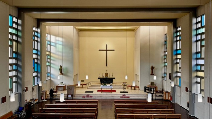 Moderne Kircheninnenausstattung mit hölzernen Kirchenbänken, Kreuz und bunten Glasfenstern.