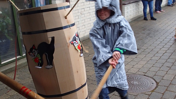 Et barn i regnfrakke og hat leger med en stor trætønde på en pæl udendørs.