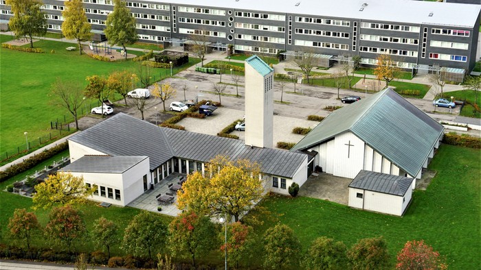 Moderne kirkekompleks omgivet af boligbygninger, parkeringsområde og grønne områder.