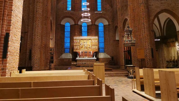 Elegant kirkeinteriør med træbænke, farvede glasvinduer og et detaljeret alter med religiøse statuer.