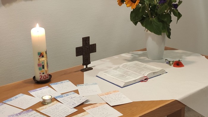 Ein Tisch mit Kerze, Kreuz und Blumen in einem Raum