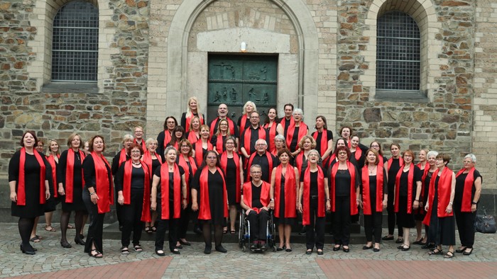 Ein großer Chor in roten Roben posiert vor einem alten Steingebäude.