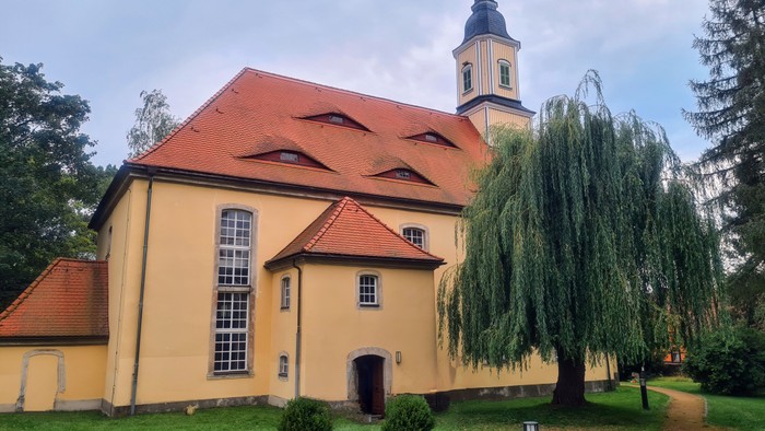 Gelbe Kirche mit hohem Turm und grüner Weide vor dem Gebäude