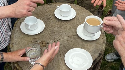 Eine Gruppe von Menschen sitzt um einen Baumstamm und trinkt Kaffee.