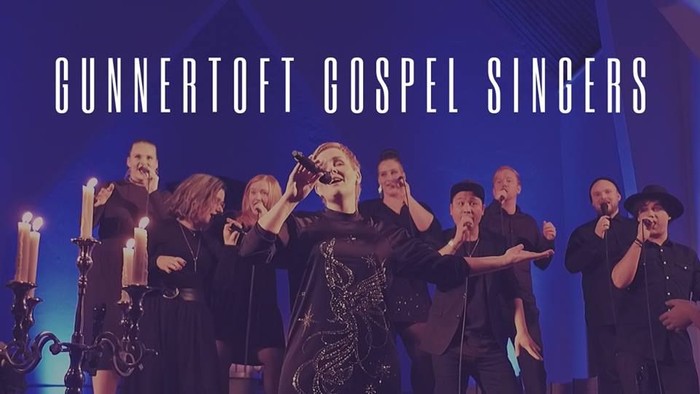 Gunnertoft Gospel Singers optræder på scenen med mikrofoner og lys.