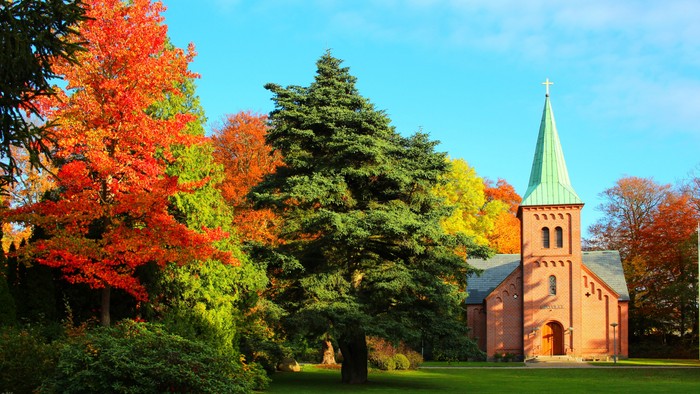 En kirke med tårn og spire, omgivet af faldende blad og grønne træer