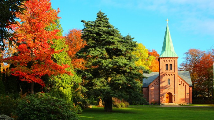 En kirke med tårn og spire, omgivet af faldende blad og grønne træer